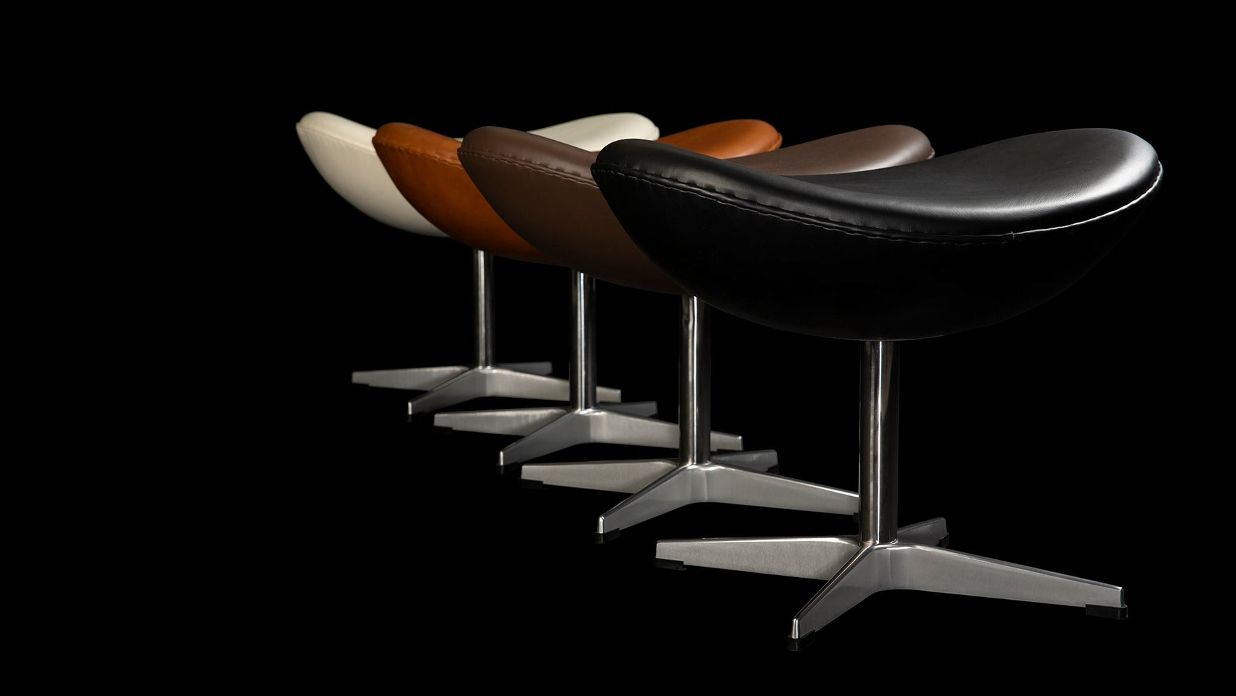 Set in a cascade of White, Tan, Brown & Black leather, the Arne Jacobsen Ottoman Stools look majestic atop a dark black background in this banner image