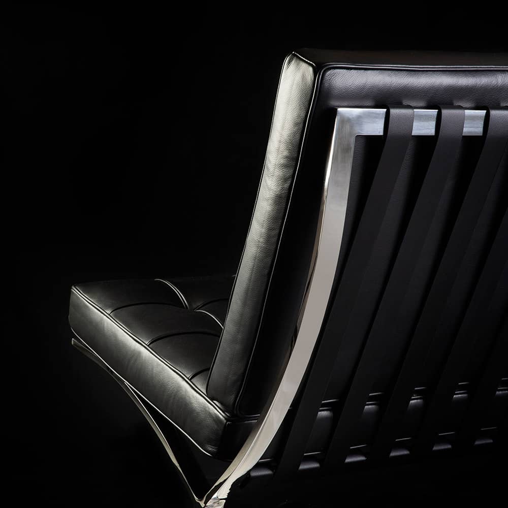 Close up rear view of black leather chrome framed Barcelona Chair on black background