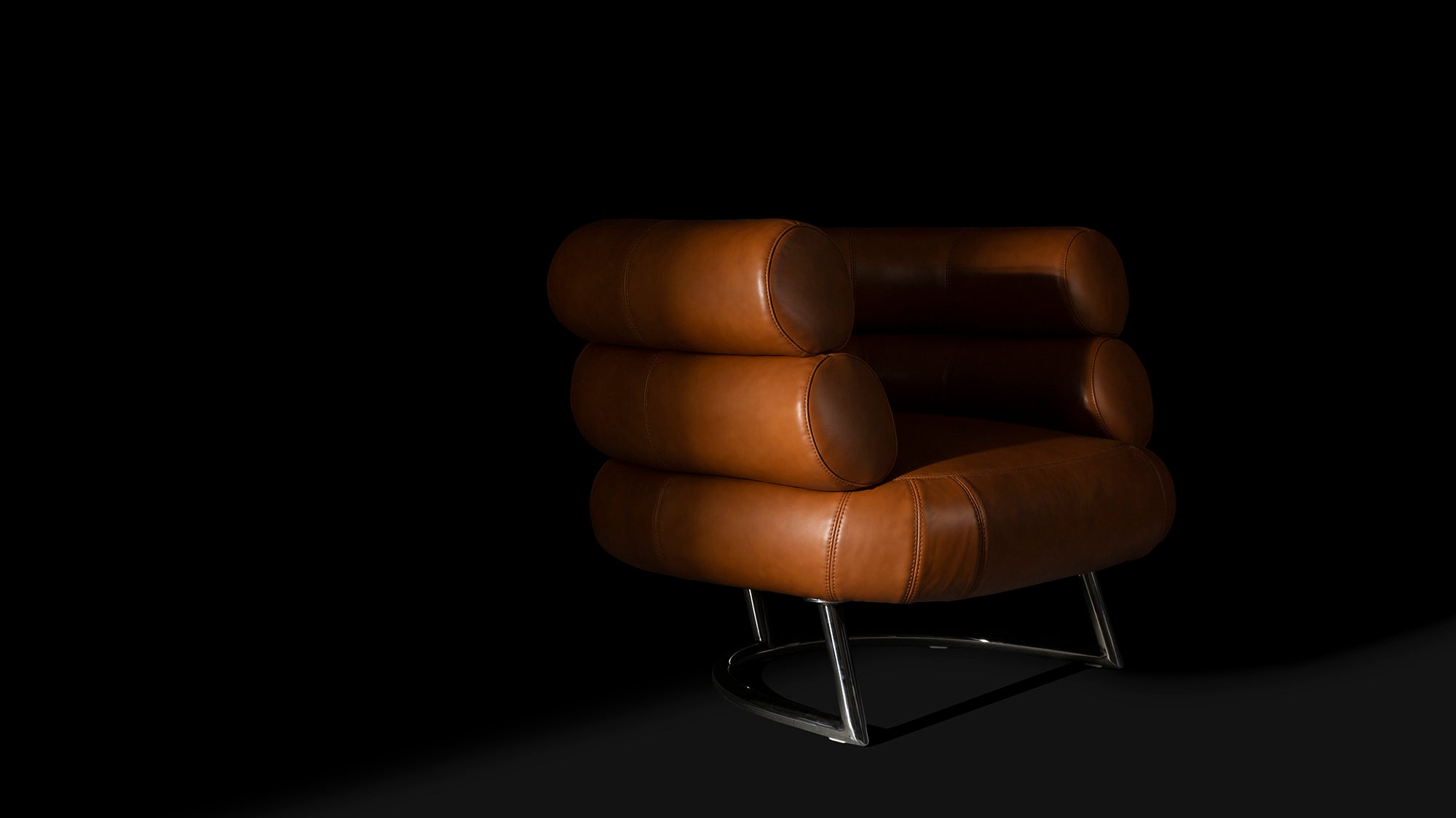 Front angled view of the tan leather Eileen Gray Bibendum Chair on a black background