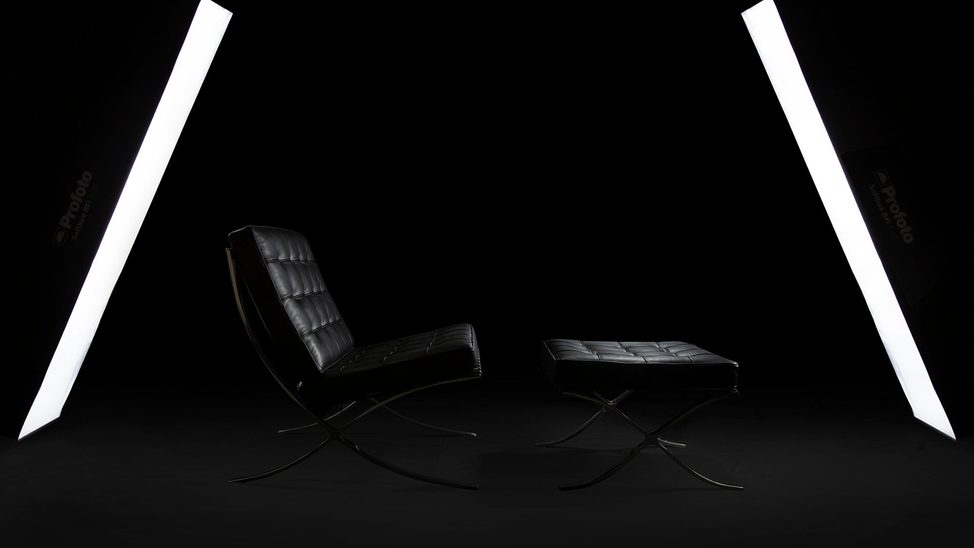A side view of the black leather Barcelona Chair & Ottoman on a black background with two lights at each end