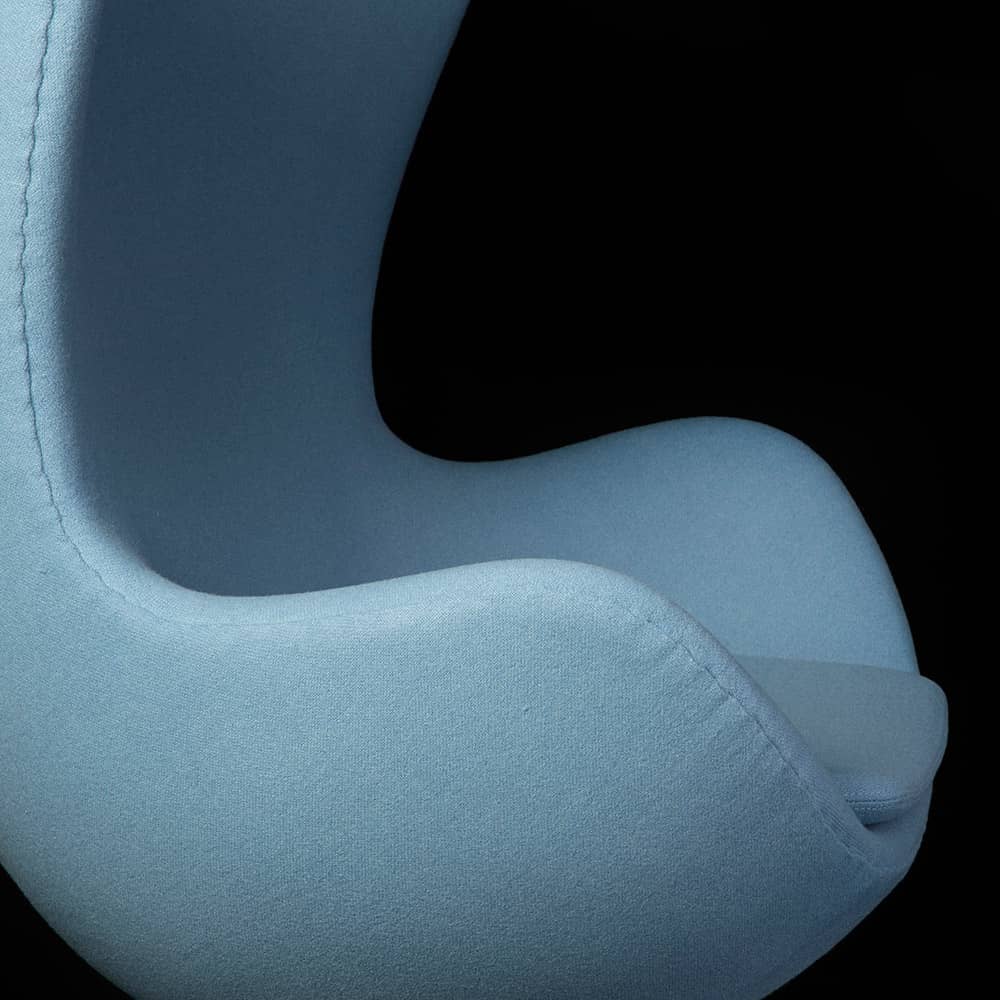 Close up side view of light blue fabric Jacobsen Egg Chair on a black background