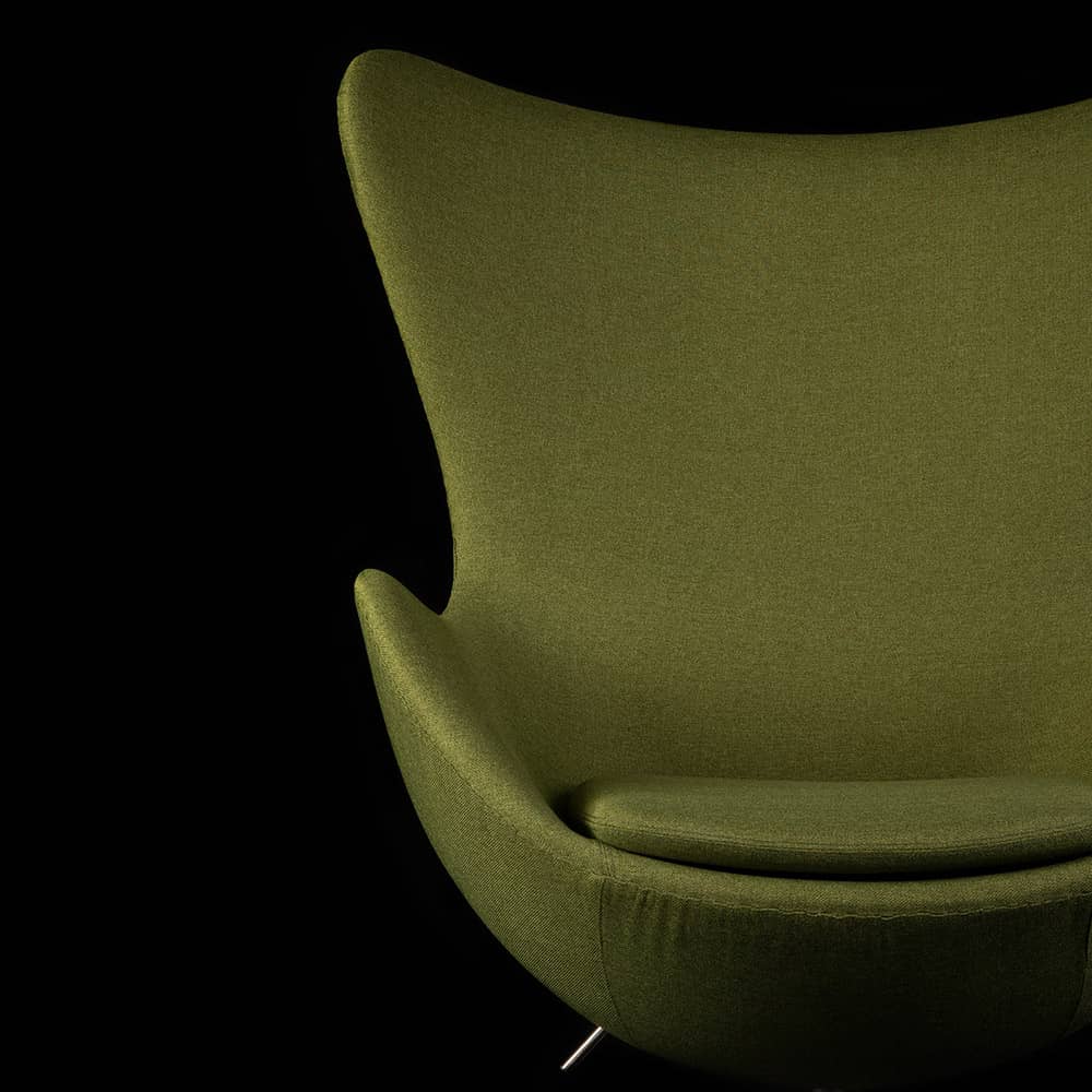 Partial front view of green fabric Arne Jacobsen Egg Chair on a black background