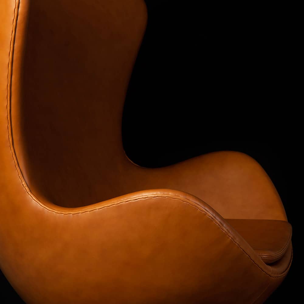 Close up side view of the Tan Leather Jacobsen Egg Chair on a black background