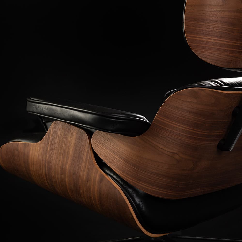 Close up rear angled view of black and walnut Eames Lounge Chair on black background