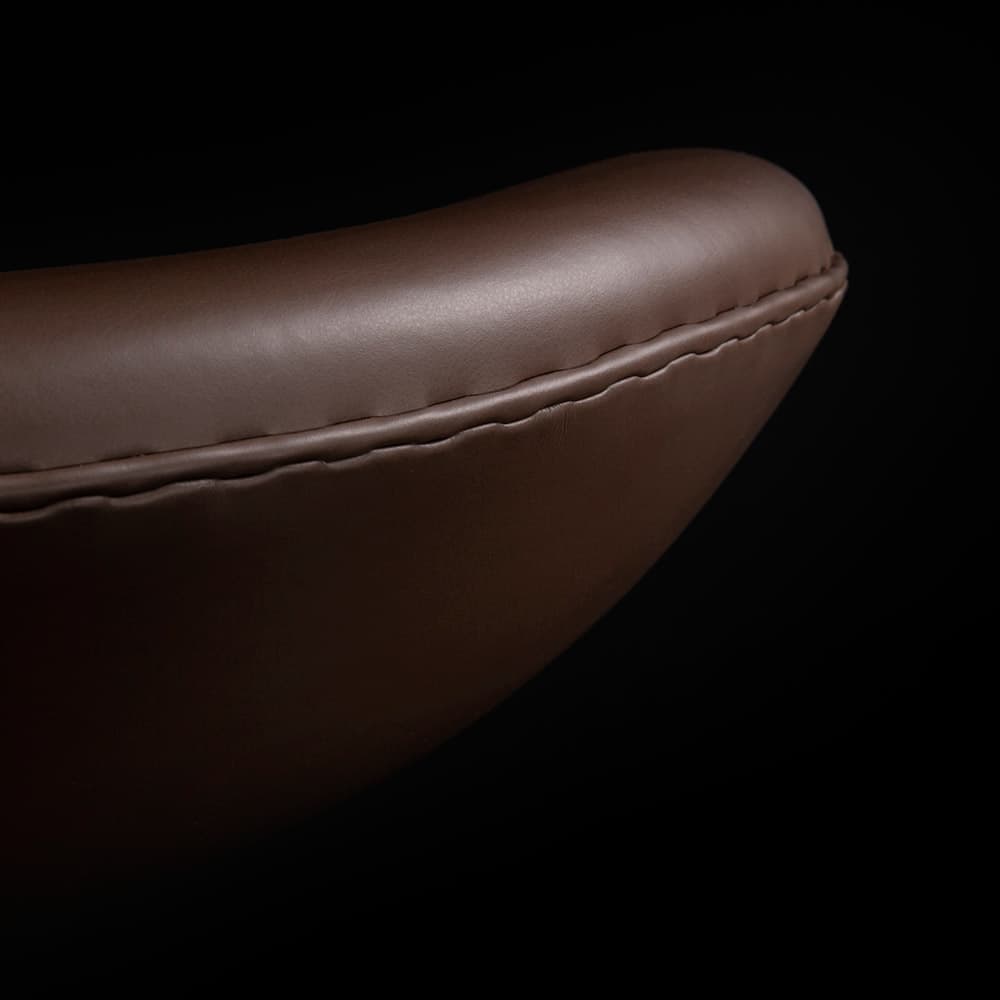 Close up front view of brown leather Arne Jacobsen Ottoman Stool on a black background