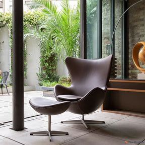 Front angled view of brown leather Jacobsen Egg Chair & Ottoman shown in a living space