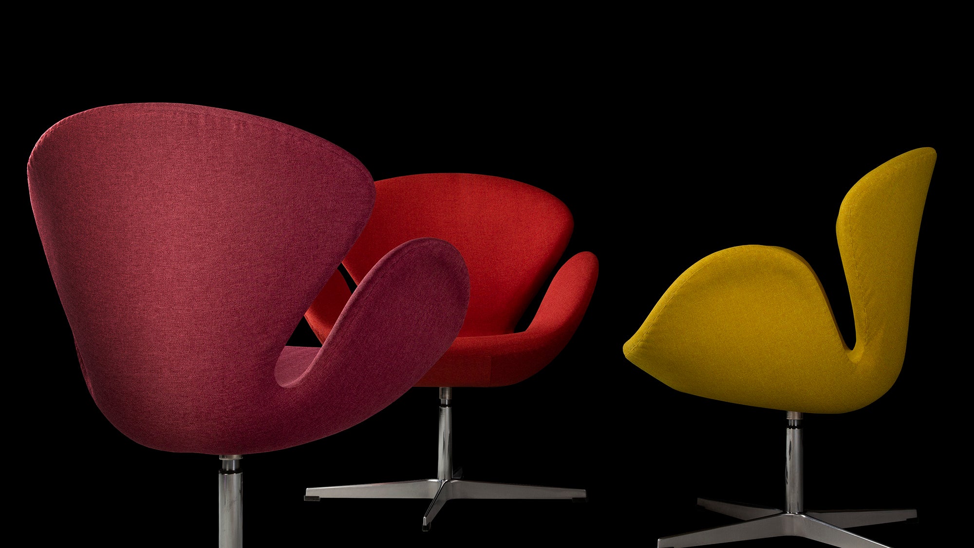 Pink, red and yellow Jacobsen Swan Chairs from rear, front and side on a black background   