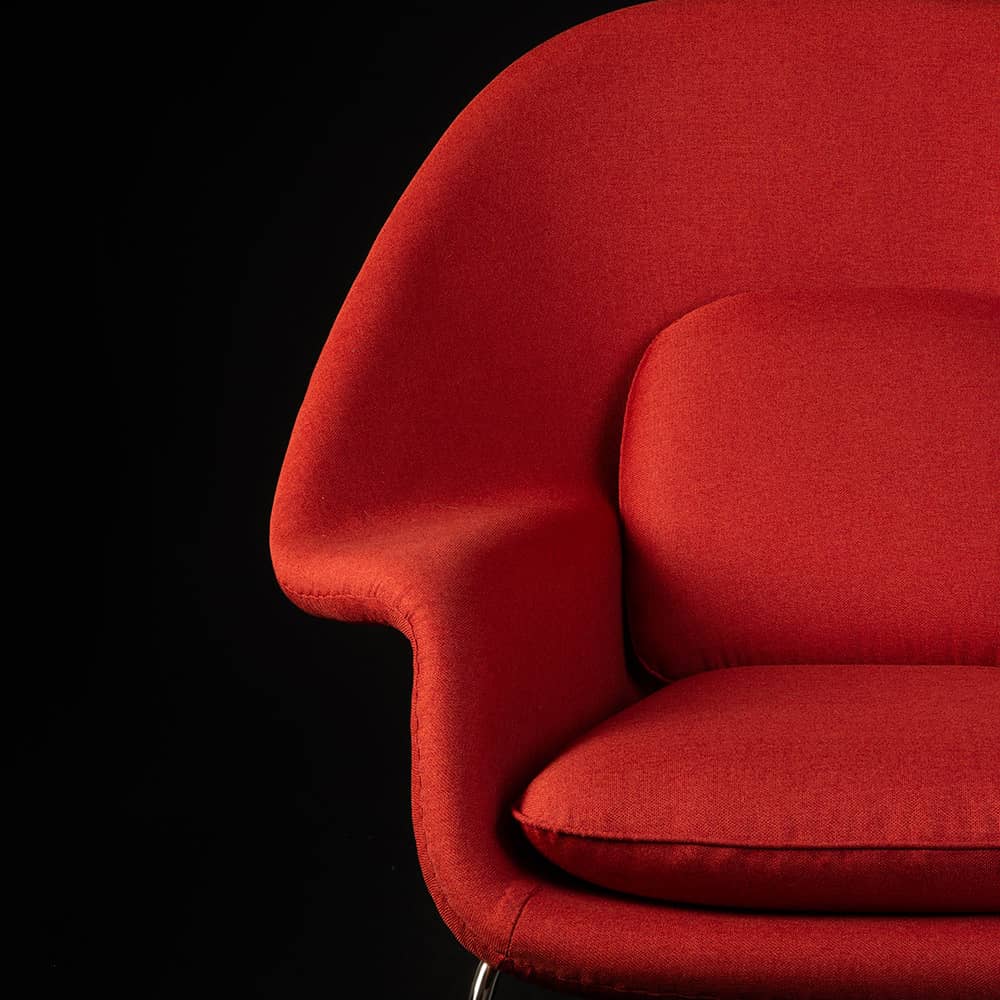 Partial front view of the red fabric Eero Saarinen Womb Chair on black background