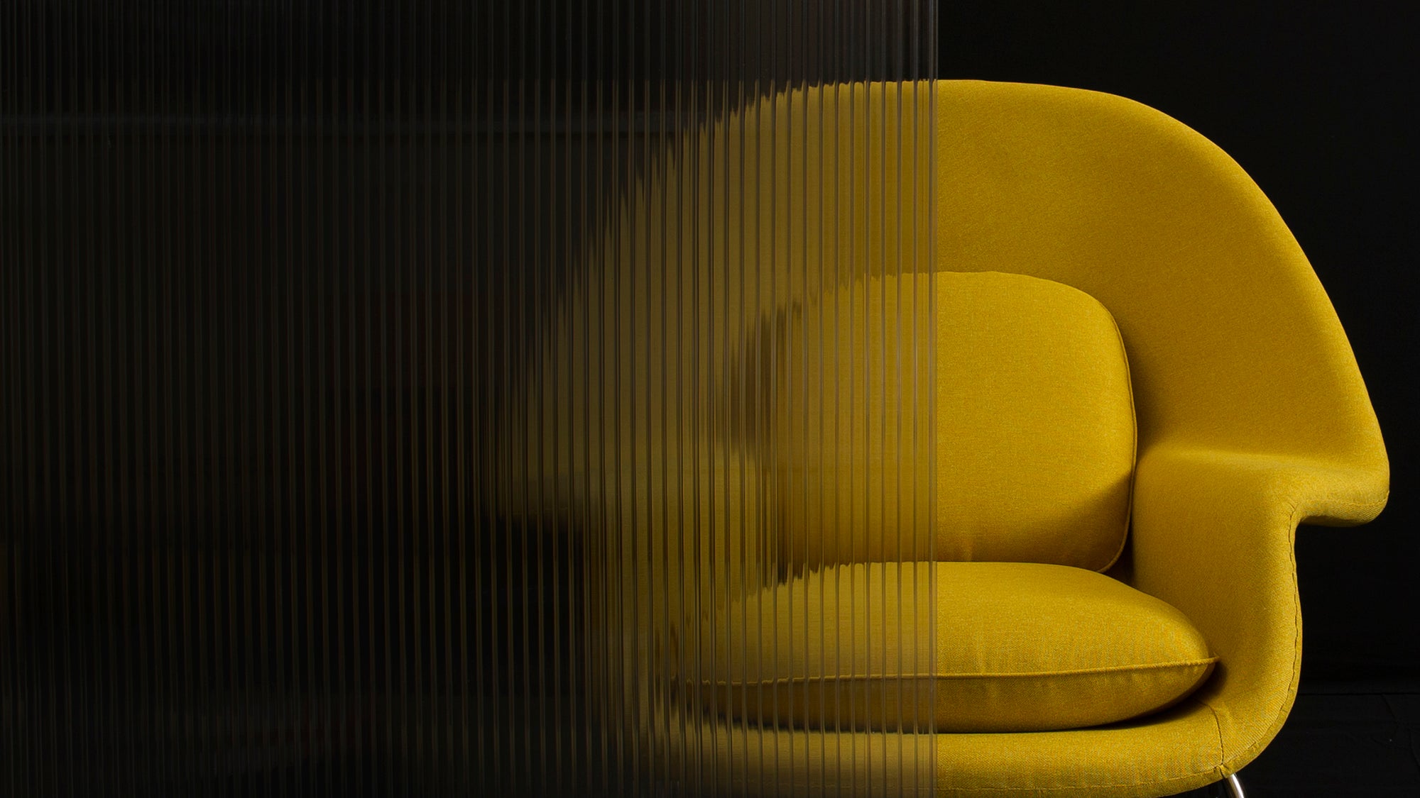 Front view of a yellow fabric Eero Saarinen Womb Chair half hidden by a semi transparent screen