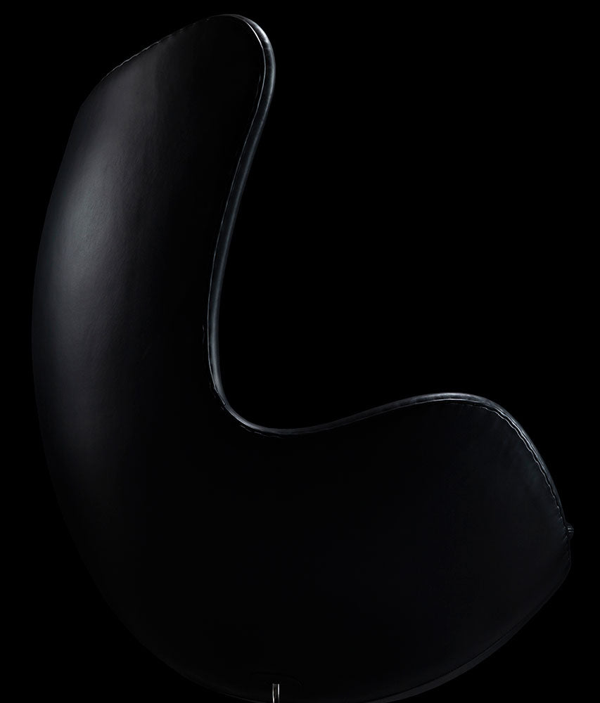 Right side view of the black leather Arne Jacobsen Egg Chair on a black background